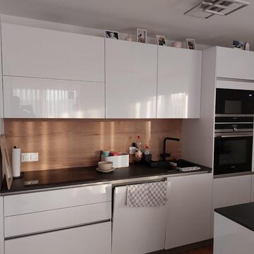 Moderne weiße Einbauküche mit Hochglanzfronten, Holzrückwand und integrierten Siemens-Geräten in einer NEBAU-Wohnung in Eisenstadt