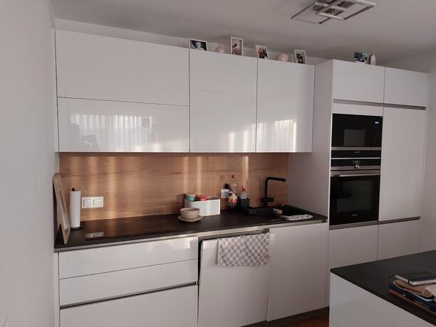 Moderne weiße Einbauküche mit Hochglanzfronten, Holzrückwand und integrierten Siemens-Geräten in einer NEBAU-Wohnung in Eisenstadt