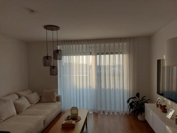 Wohnzimmer mit cremefarbenem Sofa, TV-Möbel und bodentiefen Balkonfenstern mit transparenten Vorhängen