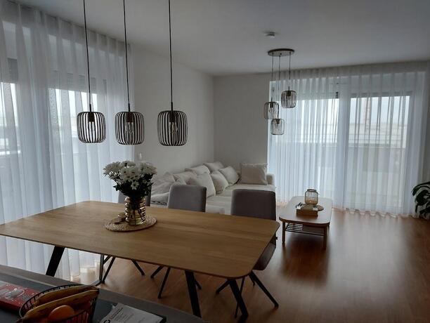 Offener Wohn-Ess-Bereich mit Eichentisch, weißem Sofa und großen Panoramafenstern in einer NEBAU-Wohnung Eisenstadt