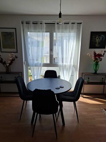 Esszimmertisch im Wohn-Essbereich, runder Tisch mit vier Sesseln dahinter ein Fenster und Bilder links und rechts neben dem Fenster
