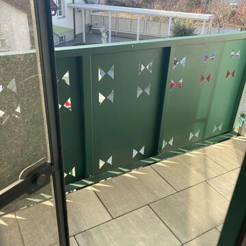 Wohnung Deutschkreutz Balkon – grünes Metallgeländer mit Dreiecksausschnitten und Blick über die Ortschaft.