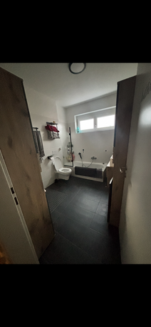Gäste-WC der Maisonettewohnung in Neudörfl mit Badewanne und dunklem Fliesenboden