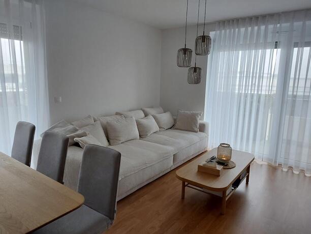 Großzügiges Wohnzimmer mit hellem Cord-Sofa, Holzcouchtisch und bodentiefen Fenstern mit Balkonzugang