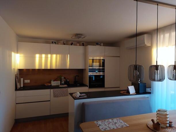 Wohnküche mit weißer Einbauküche, Kücheninsel und offener Verbindung zum Wohnbereich im Abendlicht