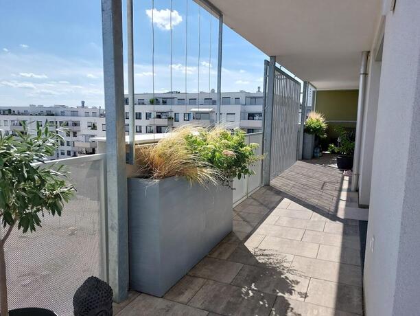 Großzügiger Balkon mit Betonplatten, Glasbrüstung und begrünten Pflanztrögen mit Weitblick