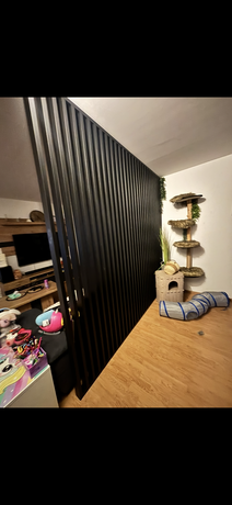 Wohnbereich im Obergeschoss mit dekorativem Lamellen-Raumteiler in Schwarz und Holzboden